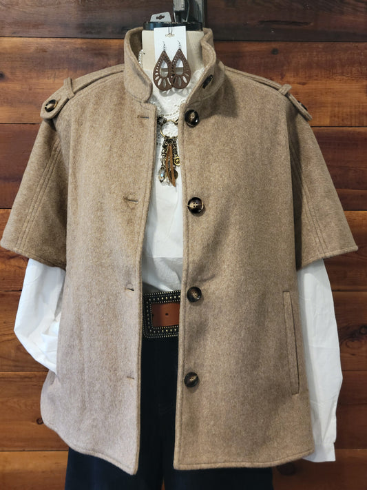 A Toffee short-sleeve cape jacket with a high stand collar and dark buttons, styled over a white shirt and dark pants on a hanger against a wooden wall.