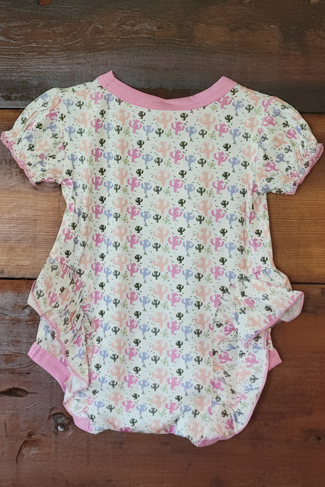 cactus-patterned baby romper with pink trim on a wooden surface