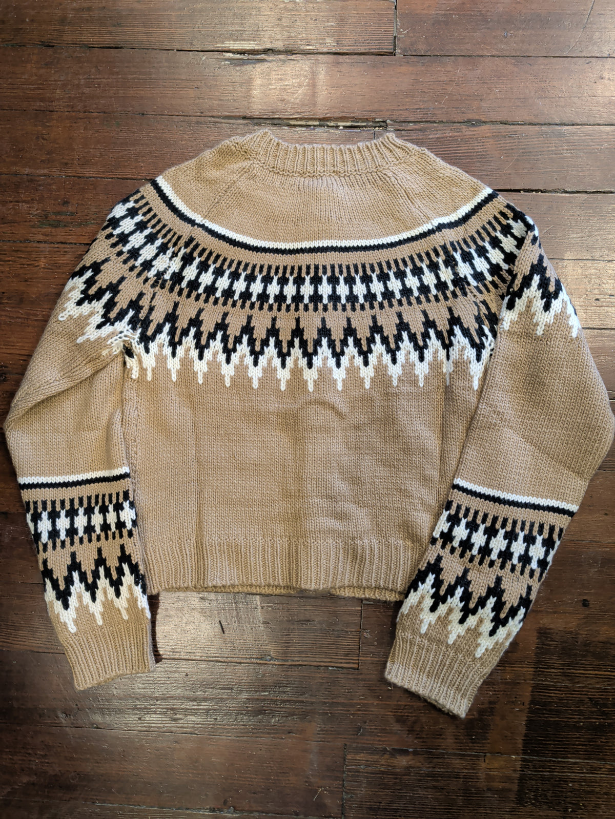 Back of light brown Fair Isle cardigan showing black and cream patterning across the shoulders and lower sleeves.