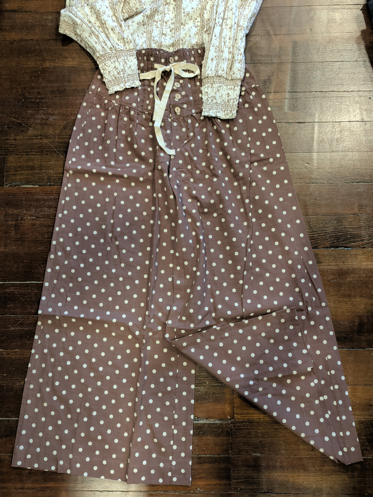 Brown wide leg pants with cream polka dots, front buttons, and a cream waist tie laid flat with a floral blouse.