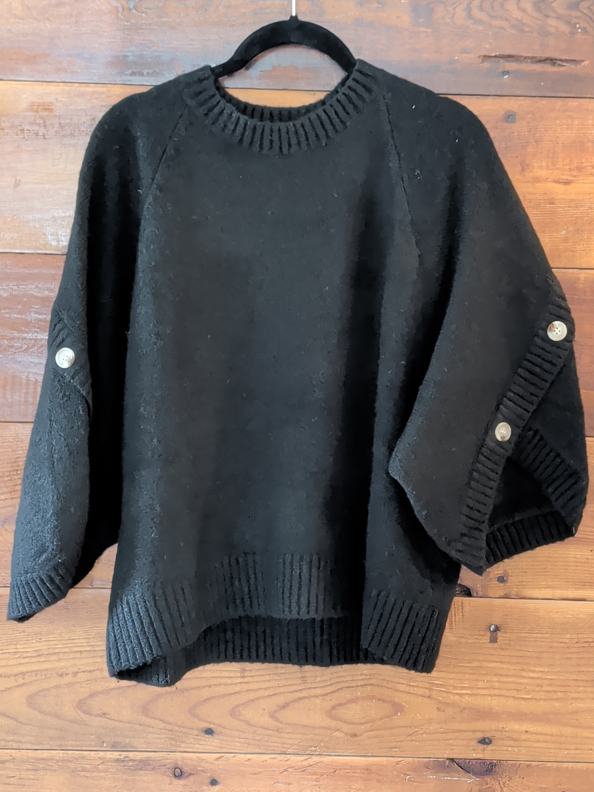 Black knit pullover on a hanger, showing a ribbed round neckline, wide button-accent sleeves, and ribbed hem.