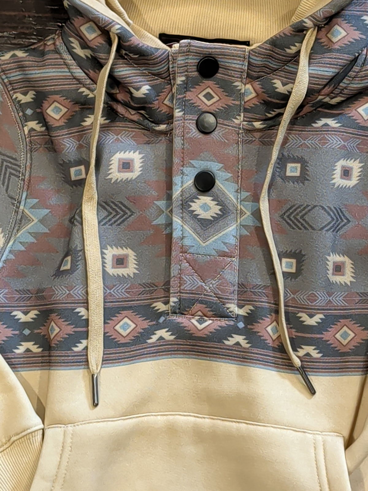 Close-up of the hoodie’s closed snap-front placket, Southwestern geometric print, and cream hood drawstrings