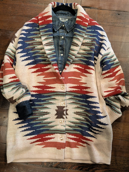Cream Southwestern-pattern button-front cardigan in rust, navy, sage, and brown, layered over a denim shirt.