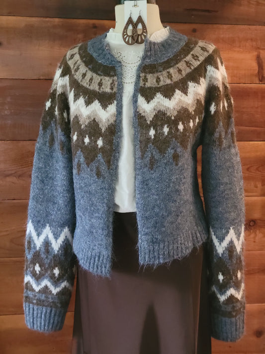 A fuzzy knit cardigan sweater with a brown, gray, and white Fair Isle pattern, displayed on a mannequin torso against a wooden wall background.