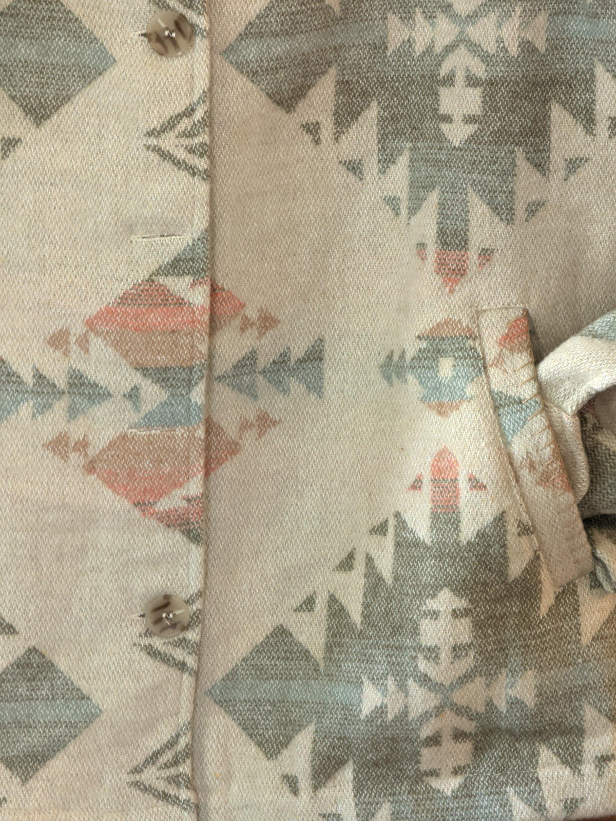 Close-up of the cream Southwestern print coat showing a side pocket and muted sage, blue, and peach geometric motifs