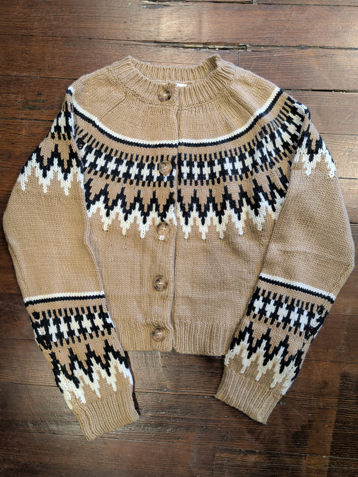 Front of light brown Fair Isle cardigan with black and cream patterned shoulders and sleeves, buttons, and ribbed trim.