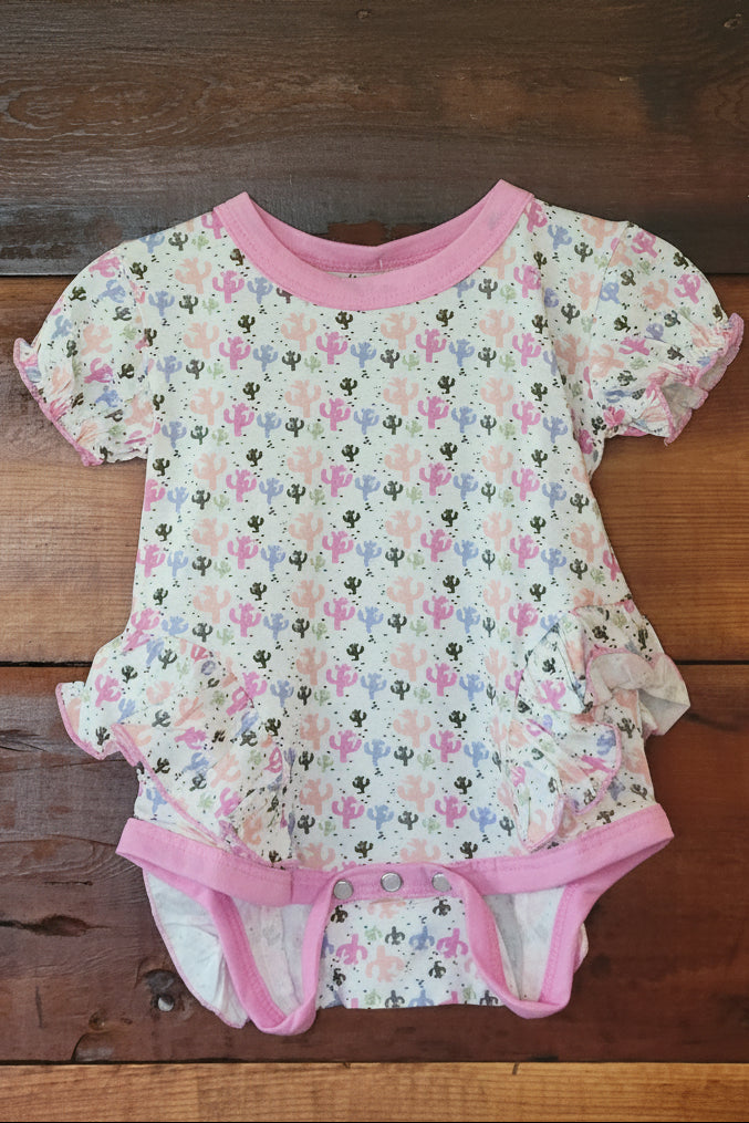 Cactus baby onesie with pink trim on a wooden surface