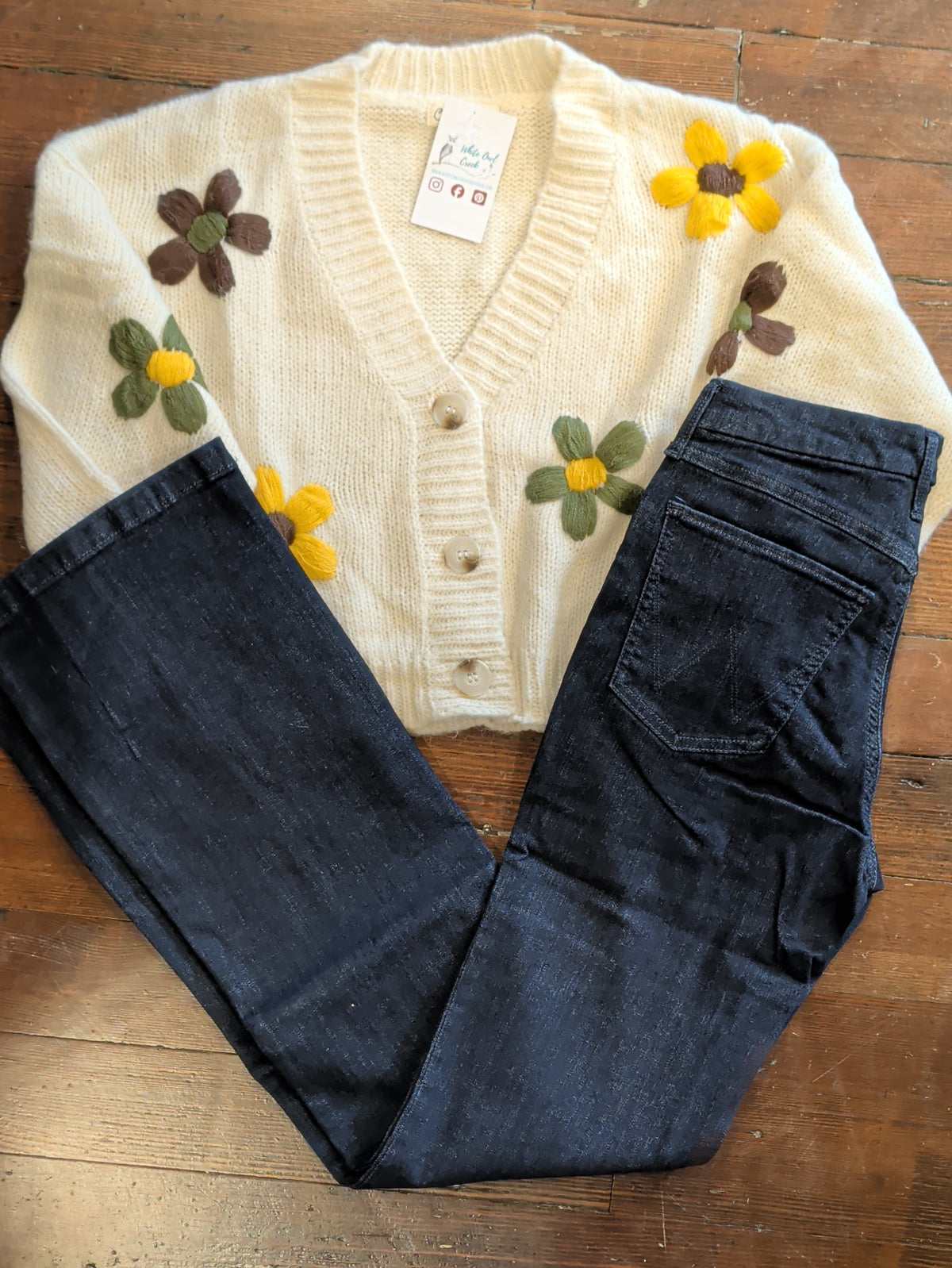 Close flat lay of Wrangler Bespoke Camryn dark blue jeans with a cream floral cardigan.