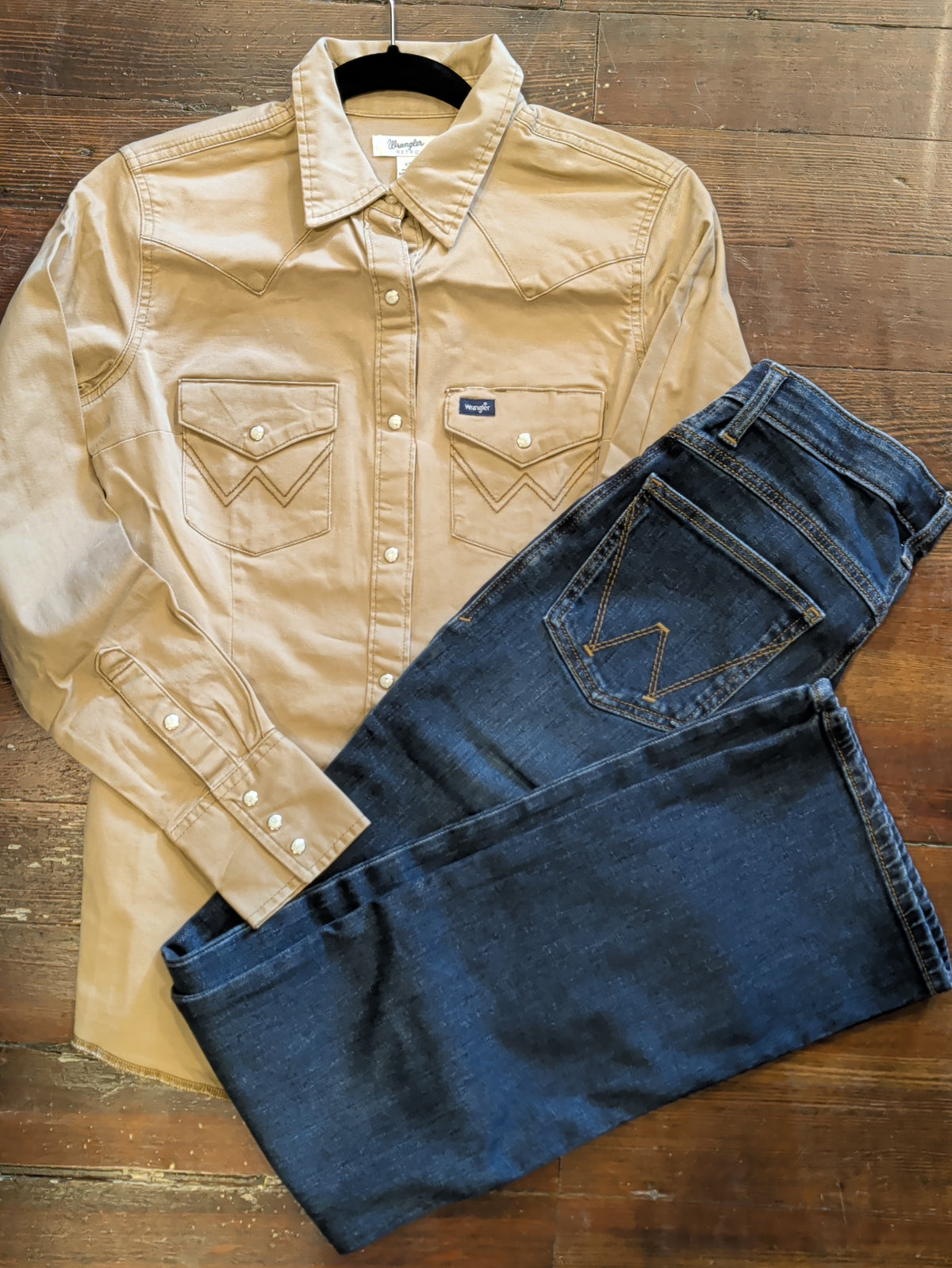 Wrangler Rawhide women’s Western snap shirt styled with dark blue jeans on a wooden background.