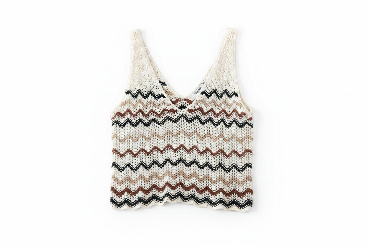 A relaxed knit crochet vest with a zigzag chevron pattern in cream, tan, brown, and black, laid flat on a dark wood plank background.