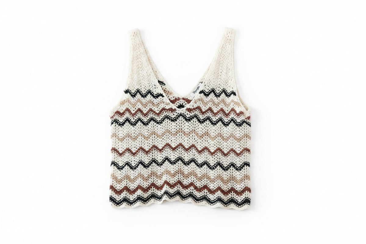 A relaxed knit crochet vest with a zigzag chevron pattern in cream, tan, brown, and black, laid flat on a dark wood plank background.
