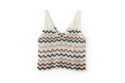 A relaxed knit crochet vest with a zigzag chevron pattern in cream, tan, brown, and black, laid flat on a dark wood plank background.