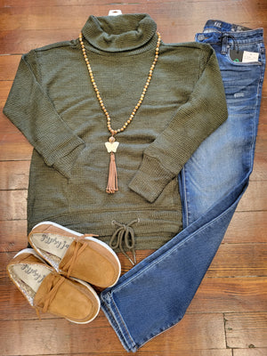 olive turtle neck pullover with kangaroo pocket paired with denim jeans and brown shoes with beaded necklace